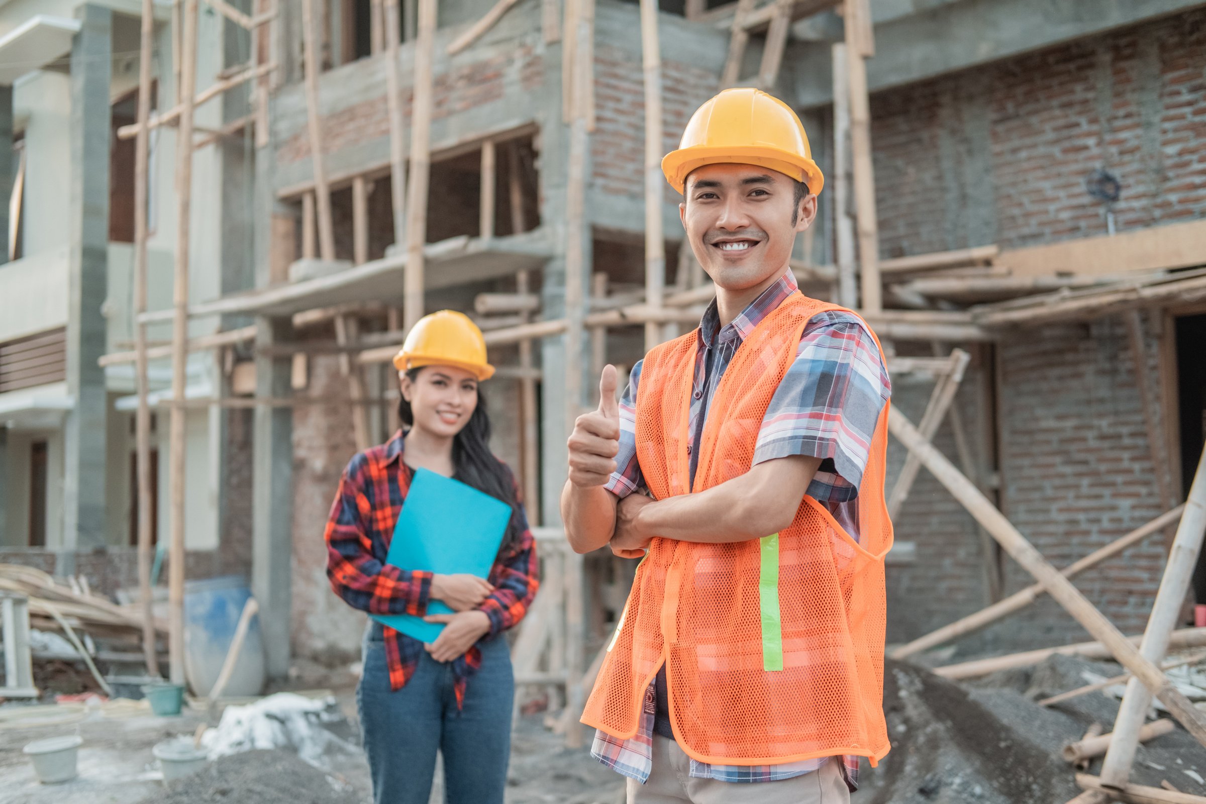 Asian Male Contractor Stands with Crossed Hands Smiling at the Camera Wearing a Safety Helmet